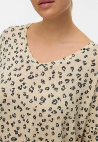 Pull à imprimé léopard avec un col en V, fabriqué dans un tissu léger ; présente une base crème avec des taches noires réparties sur toute la surface.