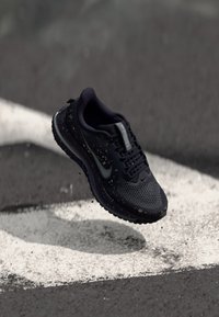 Nike teka za tek v temno modri barvi s zračnim mrežastim zgornjim delom, teksturiranim podplatom in odsevnimi poudarki. Vključuje podrobnosti s kapljanjem barve.