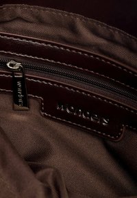 Primer plano del interior de tela marrón con una etiqueta de cuero cosida y un tirador de cremallera grabado con la palabra "wonders".