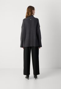 Pull ample gris foncé avec un col haut, un ourlet côtelé et un détail de couture au dos, associé à un pantalon large noir et des talons noirs.
