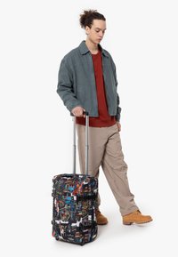 Plecak na kółkach z czarnym materiałem z kolorowymi wzorami graffiti. Posiada regulowane paski i solidny uchwyt. Jasna, trwała podstawa.