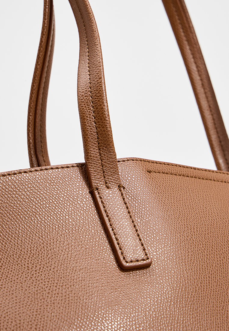 Brązowa skórzana torba tote o teksturowanej powierzchni, z podwójnymi długimi uchwytami i wyraźnym kształtem. Prosty, minimalistyczny design bez ozdób.