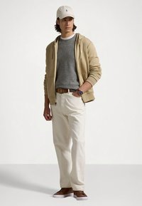 Μπεζ φούτερ με κουκούλα, γκρι πουλόβερ, λευκό παντελόνι, καφέ παπούτσια. Ανοιχτόχρωμο καπέλο του μπέιζμπολ. Casual εμφάνιση με ομαλή υφή και χαλαρή εφαρμογή.