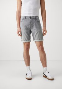Pantalones cortos de mezclilla gris claro con dobladillos enrollados, diseño de cinco bolsillos, cremallera y un botón negro. Combinados con zapatillas blancas y calcetines de caña alta.