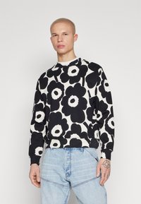 Svart-hvitt blomstermønstrete sweatshirt med rund hals og ribbede mansjetter, kombinert med lyseblå denimjeans.