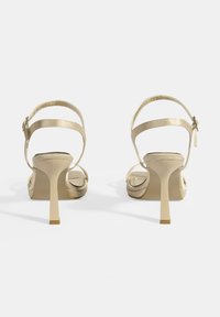 Beige Satin High Heels mit zwei Riemen über dem Knöchel, offenes Zehendesign und schmalem Stiletto-Absatz. Glatte Oberfläche und minimale Akzente.