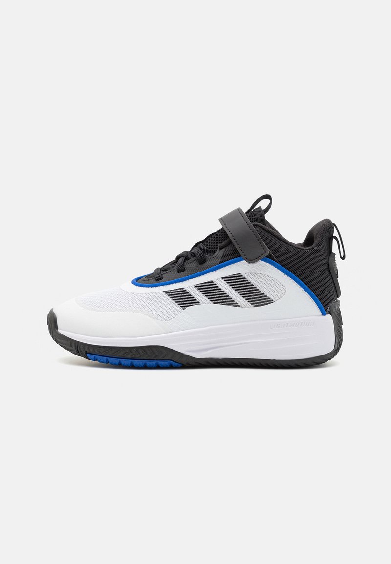 Scarpa da ginnastica bianca e nera con accenti blu, parte superiore in rete e suola in gomma. Presenta una chiusura con velcro e motivi texture lungo i lati.