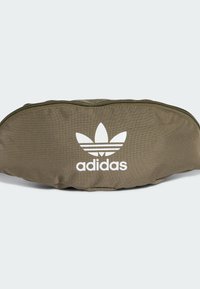Riñonera de tela verde oliva con forma curva, que presenta un logo blanco de Adidas y tres franjas horizontales. Cierre de cremallera en la parte superior.