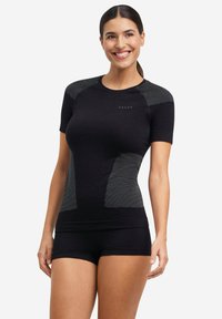 Czarny sportowy top z krótkimi rękawami, ozdobiony paskami na ramionach, dopasowany fason i przewiewna faktura. W zestawie z czarnymi szortami.