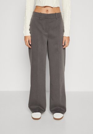 Pantaloni grigi a gamba larga realizzati in un tessuto testurizzato, con un design sartoriale, tasche laterali e una parte anteriore piatta, abbinati a scarpe bianche.
