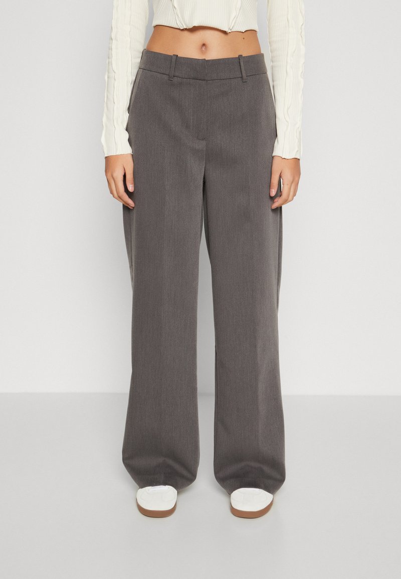 Pantaloni grigi a gamba larga realizzati in un tessuto testurizzato, con un design sartoriale, tasche laterali e una parte anteriore piatta, abbinati a scarpe bianche.