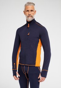 Marineblå og orange langærmet jakke med høj krave, fuld lynlås, brystlomme og kontrasterende syninger. Glat tekstur med atletisk pasform.