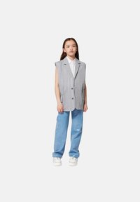 Blazer senza maniche a righe grigie con due tasche frontali, chiusura a bottoni, abbinato a pantaloni larghi azzurri e sneakers bianche.