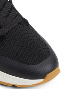 Chaussure de sport noire avec tige en tissu en maille, revêtement synthétique texturé et semelle extérieure en caoutchouc. Dispose d'une adhérence flexible et d'un col rembourré.