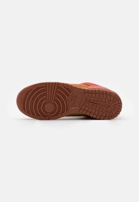 Suola in gomma marrone di una sneaker Nike che mostra motivi a griglia e circolari su uno sfondo bianco.