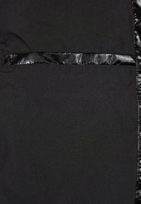 Tissu noir présentant une texture lisse avec une rayure accentuée, glossy et à motif. Le design est simple et uniforme, avec un détail de poche.