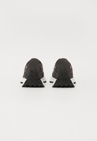 Schwarze Wildledersneaker mit weißen Sohlen, die eine dreieckige Fersenform, eine strukturierte Gummisohle und minimalistische Nähte aufweisen.