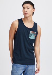 Námornícky modrý tielko s okrúhlym výstrihom, ktorý má vzorovanú vrecko s tropickými dizajnovými prvkami. Mäkka látka a voľný strih.