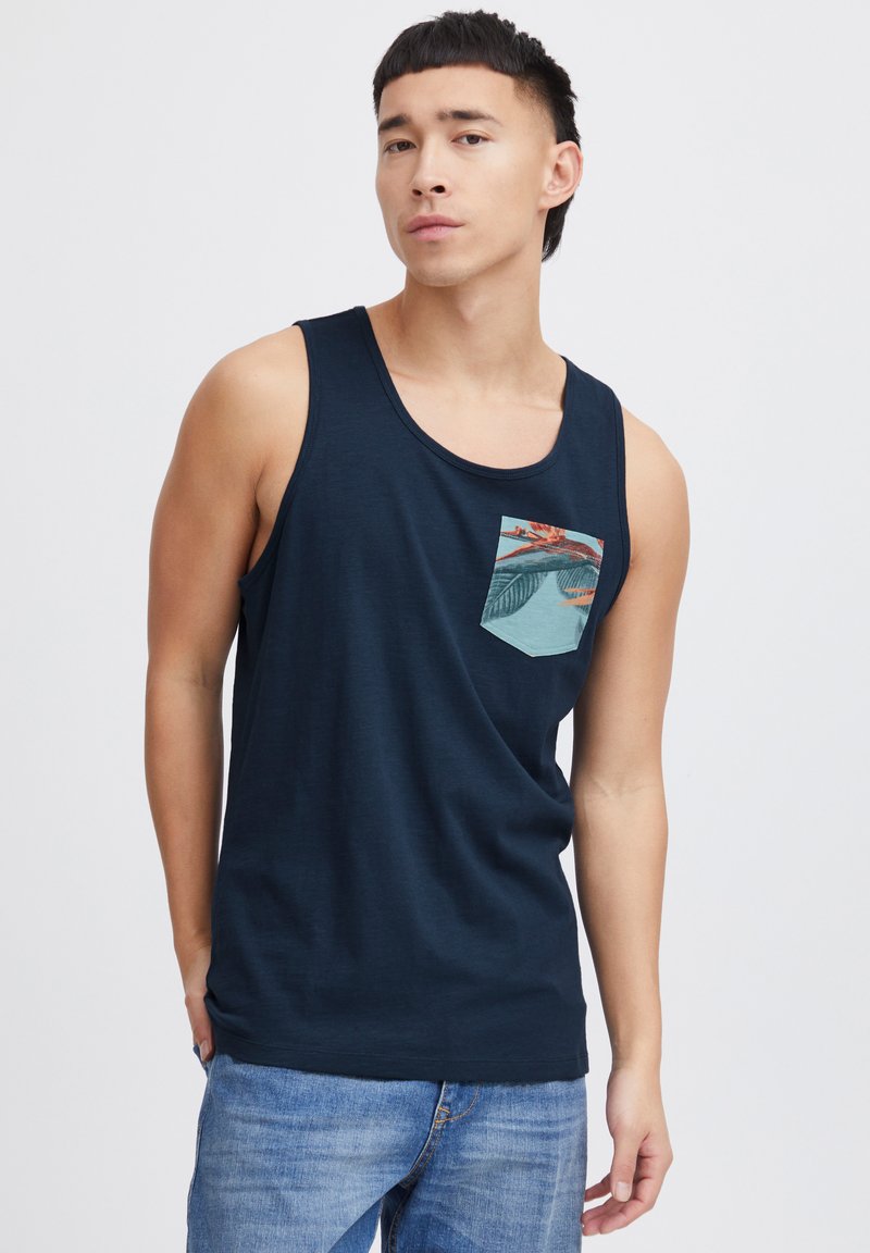 Námornícky modrý tielko s okrúhlym výstrihom, ktorý má vzorovanú vrecko s tropickými dizajnovými prvkami. Mäkka látka a voľný strih.