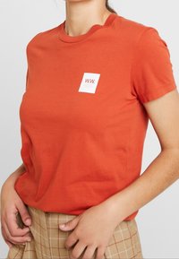 Tričko s krátkým rukávem a volným střihem v jasně oranžové barvě z bavlny, s malým bílým čtvercovým logem s "W.W." na levé části hrudi.