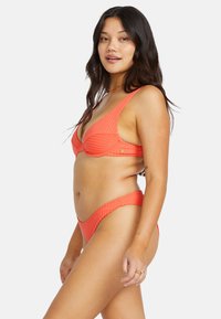 Koraal ribbel bikini set met een driehoekige bralette bovenkant en hoge taille slipjes. Beschikt over brede bandjes en subtiele gouden accenten. Zachte textuur.