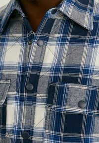 Blå och vit rutig skjorta med stort rute-mönster, knappstängning, två bröstfickor och spetsig krage. Mjuk tygstruktur.