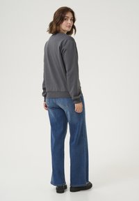 Sweatshirt gris avec un col rond, des poignets côtelés, associé à un jean bleu ample et des chaussures noires. Tissu lisse et coupe décontractée.