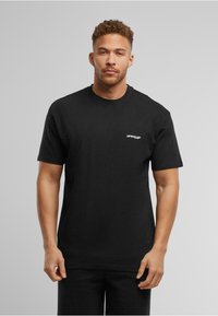 Tricou din bumbac negru cu mâneci scurte, guler rotund și text alb "UPSCALE" pe partea stângă a pieptului. Design simplu, cu o croială lejeră.