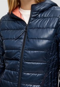 Granatowa puchowa kurtka z pikowanym wzorem, zamkiem błyskawicznym i kapturem. Posiada kontrastujące jasnoróżowe wnętrze i boczne kieszenie. Gładka, błyszcząca tekstura.