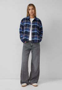 Karierter Flanellhemd in Blau, Marineblau und Weiß, mit einer lockeren Passform und Knopfverschluss. Kombiniert mit hoch taillierten grauen Jeans im weit geschnittenen Stil.