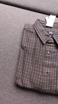 Zložen BDG Urban Outfitters karirast gumbastih srajca v vijoličnih, zelenih in bež tonih, ki počiva na sivi tkaninski površini.