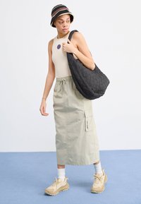 Beige tank top, világoszöld maxi szoknya, fekete steppelt válltáska, csíkos vödörkalap, bézs sportcipő fehér zoknival. Egyszerű dizájn, laza megjelenés.