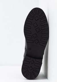 Suola di scarpa nera con motivi a presa testurizzati, taglia 38. Materiale in gomma resistente con bordo liscio e dettagli di design sottili.