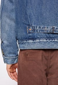 Jeansjacka i en blå nyans, med lätt slitage och knappdetaljer, parat med bruna kordflamsbyxor med en enda knapp.