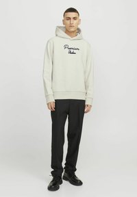 Light gray sweatshirt with a hood, featuring "Premium" embroidered in dark navy. Paired with black trousers and black shoes.