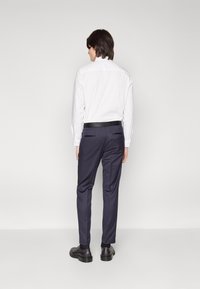 Cămașă albă cu mânecă lungă, pantaloni slim-fit navy cu talie neagră, cu manșete, textură simplă, asortați cu pantofi negri. Design minimalistic.