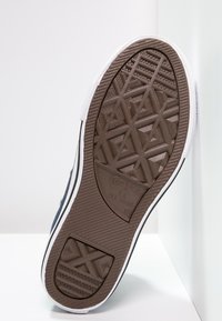 Converse sneakersula med en brun gummibotten med ett diamantmönster, vit sidostrip, och svart övre kant.