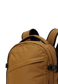Zaino in tessuto marrone con spallacci imbottiti, maniglia superiore e tasca frontale con zip. Presenta una texture liscia e dettagli di cucitura.