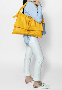 Geel leren handtas met een geknoopt ontwerp en twee grote kleppen. Het heeft één lange schouderband en een gladde textuur.