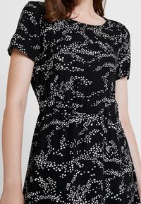 Svart klänning med ett vitt abstrakt bladmönster, korta ärmar och elastisk midja för en avslappnad passform. Slät tygkvalitet.