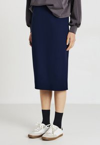 Navyblauer Midirock aus glattem Stoff, kombiniert mit weißen Sneakers, schwarzen Socken und einem grauen Sweatshirt mit gepufften Ärmeln.