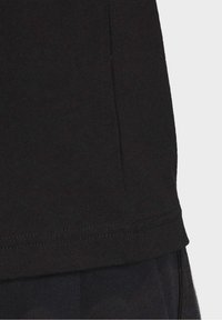 Svart bomulls-t-shirt som visar en strukturerad tygkvalitet med rundad halsringning och sydd fåll. Nära bild av sid søm-detaljen.