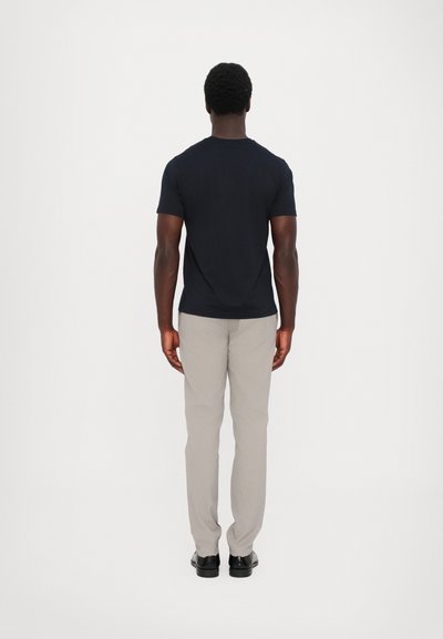 Marineblaue Baumwoll-T-Shirt mit Rundhalsausschnitt, kombiniert mit hellgrauen Hosen, von hinten betrachtet. Die Hose hat eine glatte Textur und eine schmal zulaufende Passform.