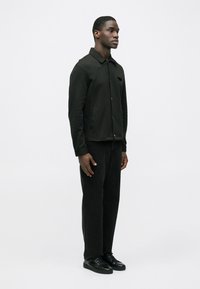 Mustast nuppudega jakk kraega, kombineeritud tumeda teksapükste ja mustade tennistega. Sile tekstuur ja minimalistlik disain.