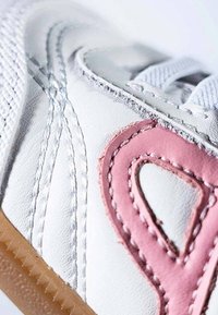 Zapatilla sintética blanca con acentos en rosa, cuero texturizado y cordones blancos. Cuenta con suela de goma y detalles cosidos.