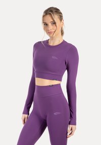 Fioletowy sportowy krótki top z długimi rękawami oraz dopasowane legginsy z wysokim stanem, ozdobione subtelnym logo. Gładka, elastyczna tkanina.