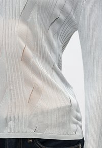 Ανοιχτό γκρι πλέκτο πουλόβερ με κατακόρυφες ραβδώσεις και μοτίβα που μοιάζουν με φύλλα. Διαθέτει ελαφρώς διαφανή υφή και εφαρμοστή σχεδίαση.