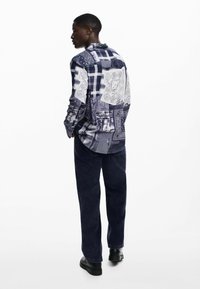 Long-sleeve shirt featuring a patchwork design in navy and white, with varying patterns, paired with dark, straight-leg pants and black shoes.