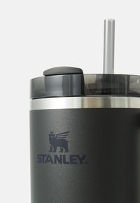 Stainless steel tumbler in matte black with a clear lid, silicone stopper, and reusable straw; features embossed Stanley logo.