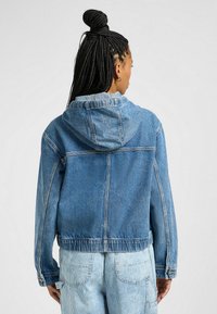 Farkkutakki hupparilla, vaaleansininen väri, rento malli, elastinen vyötärö ja näkyvät ompeluyksityiskohdat. Takakuvasta näkyy pituus ja rakenne.